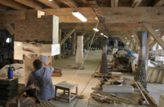 The sculptor working on a large block in a long workshop with wooden beams