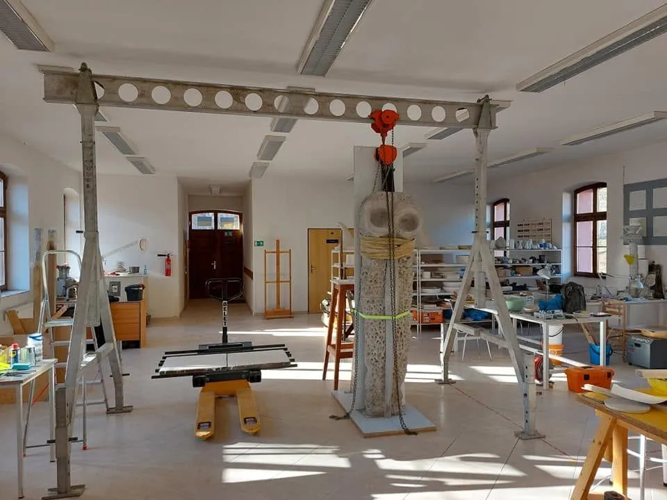 Bright workshop with a crane and a tall sculpture in progress in the middle
