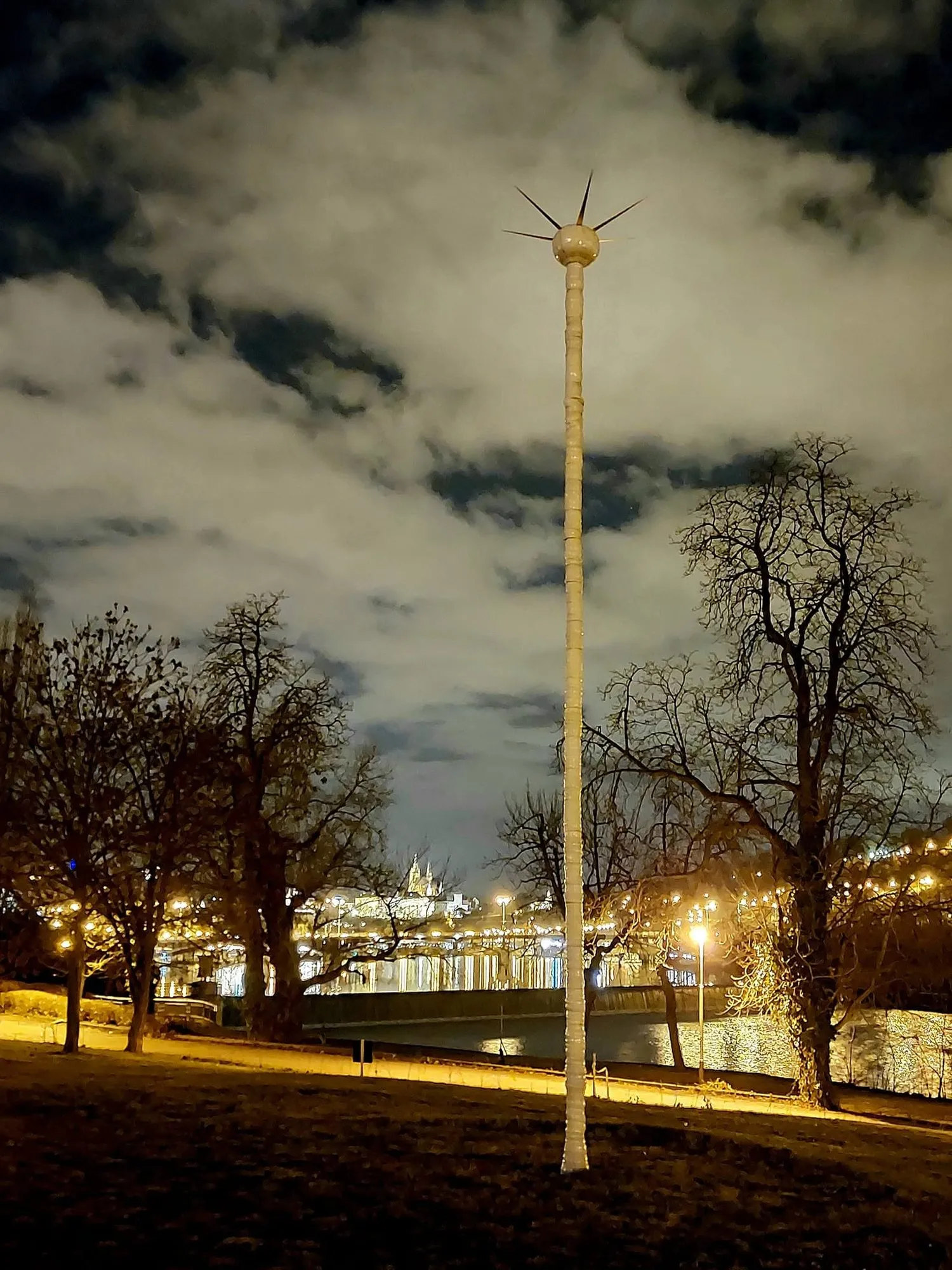 Slender white column with a radiating crown at night on the embankment