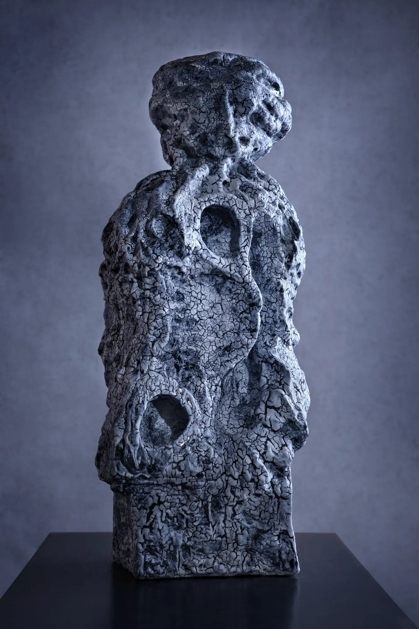 Tall blue and white ceramic sculpture with two openings on a black plinth