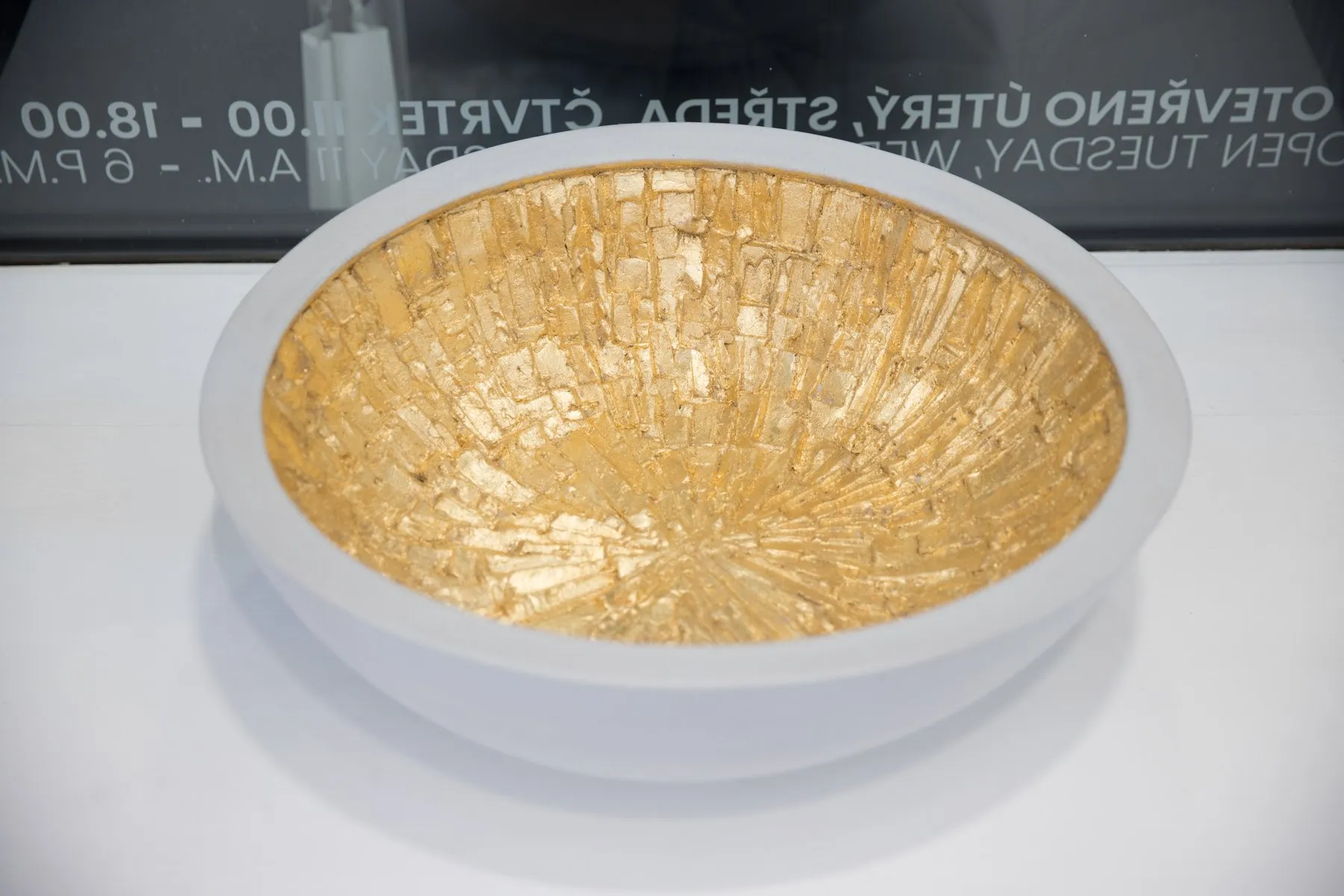 White bowl with gold mosaic inside, displayed in a showcase