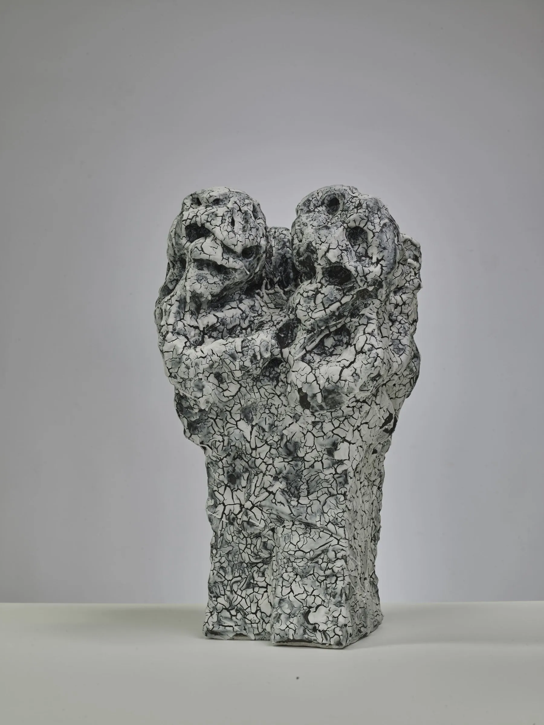 Porous two-headed sculpture with a white crackle glaze on a grey background
