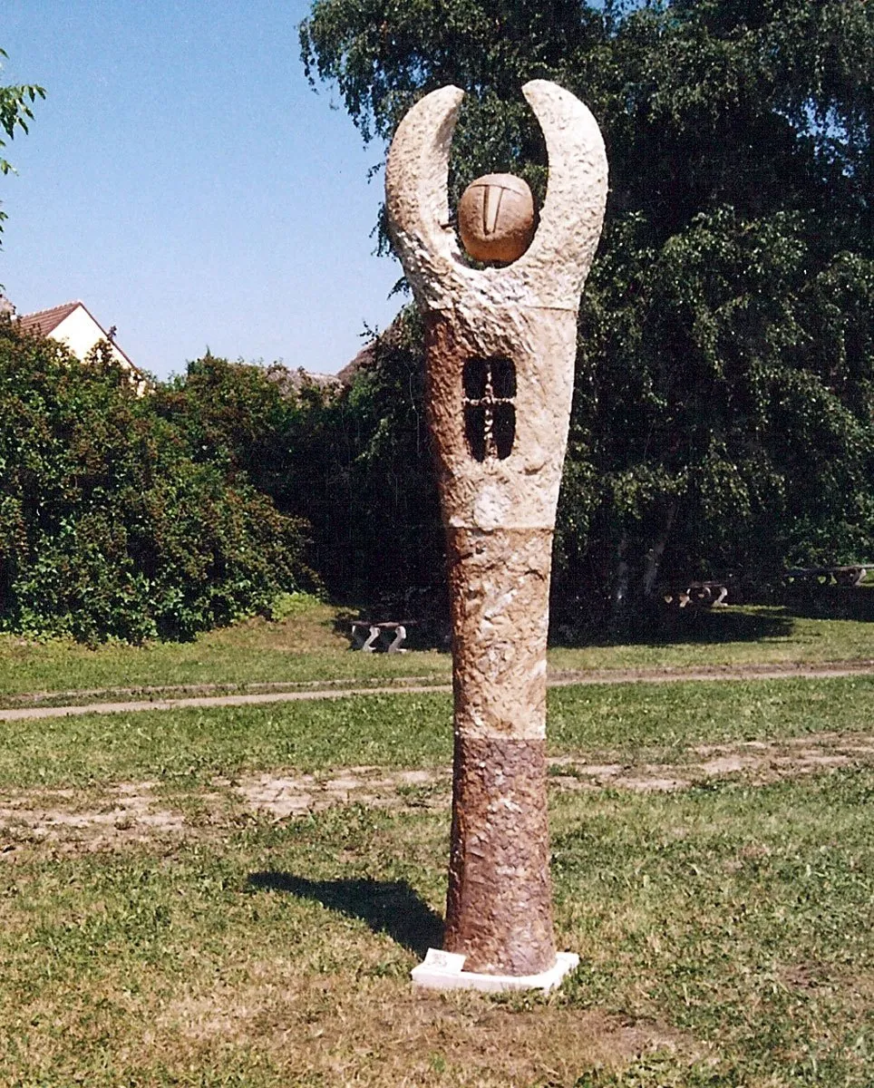 Tall sculpture with a horned head and small windows in a meadow