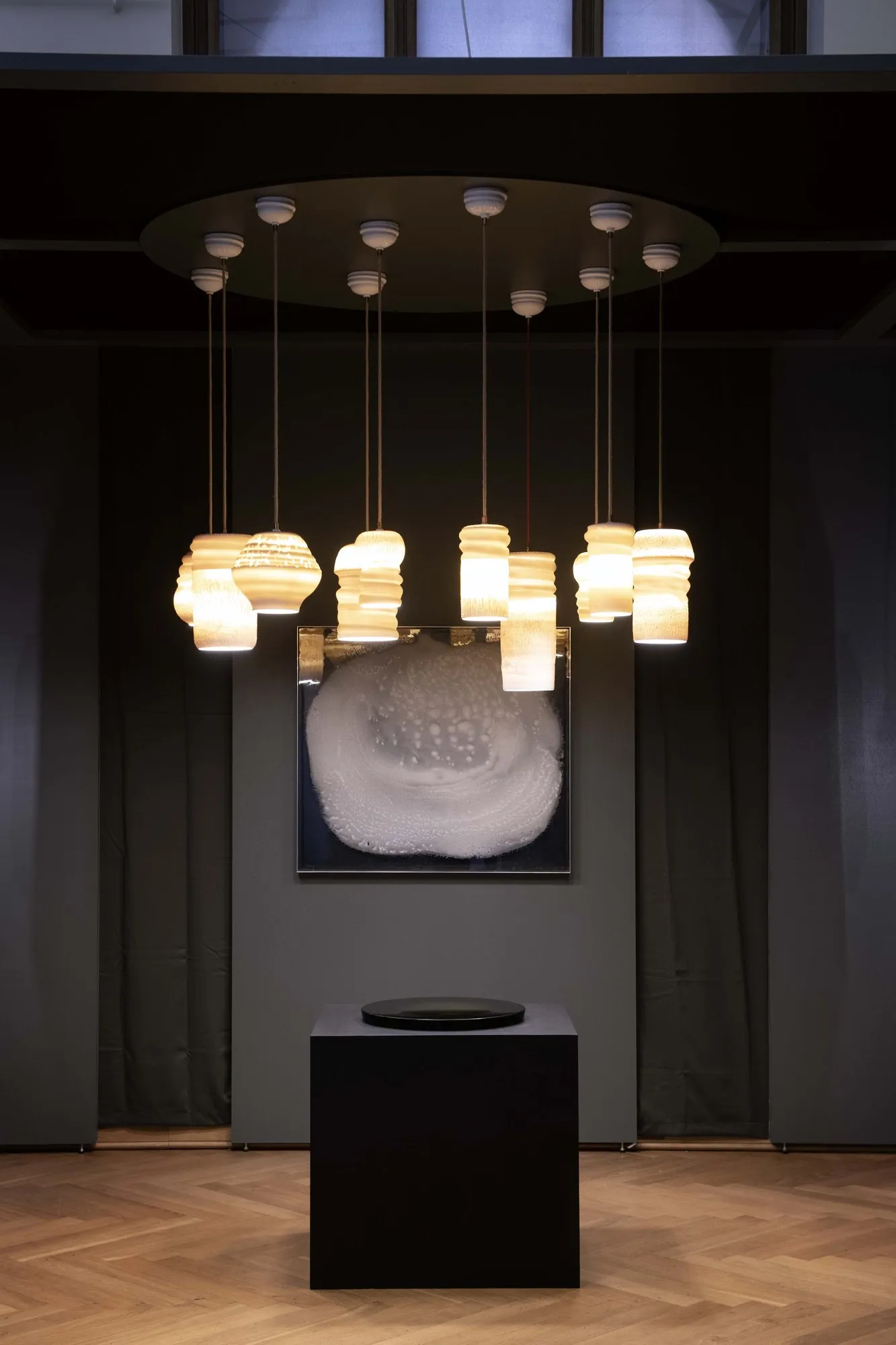 Hanging porcelain lights above a white relief and a black plinth in a dark room