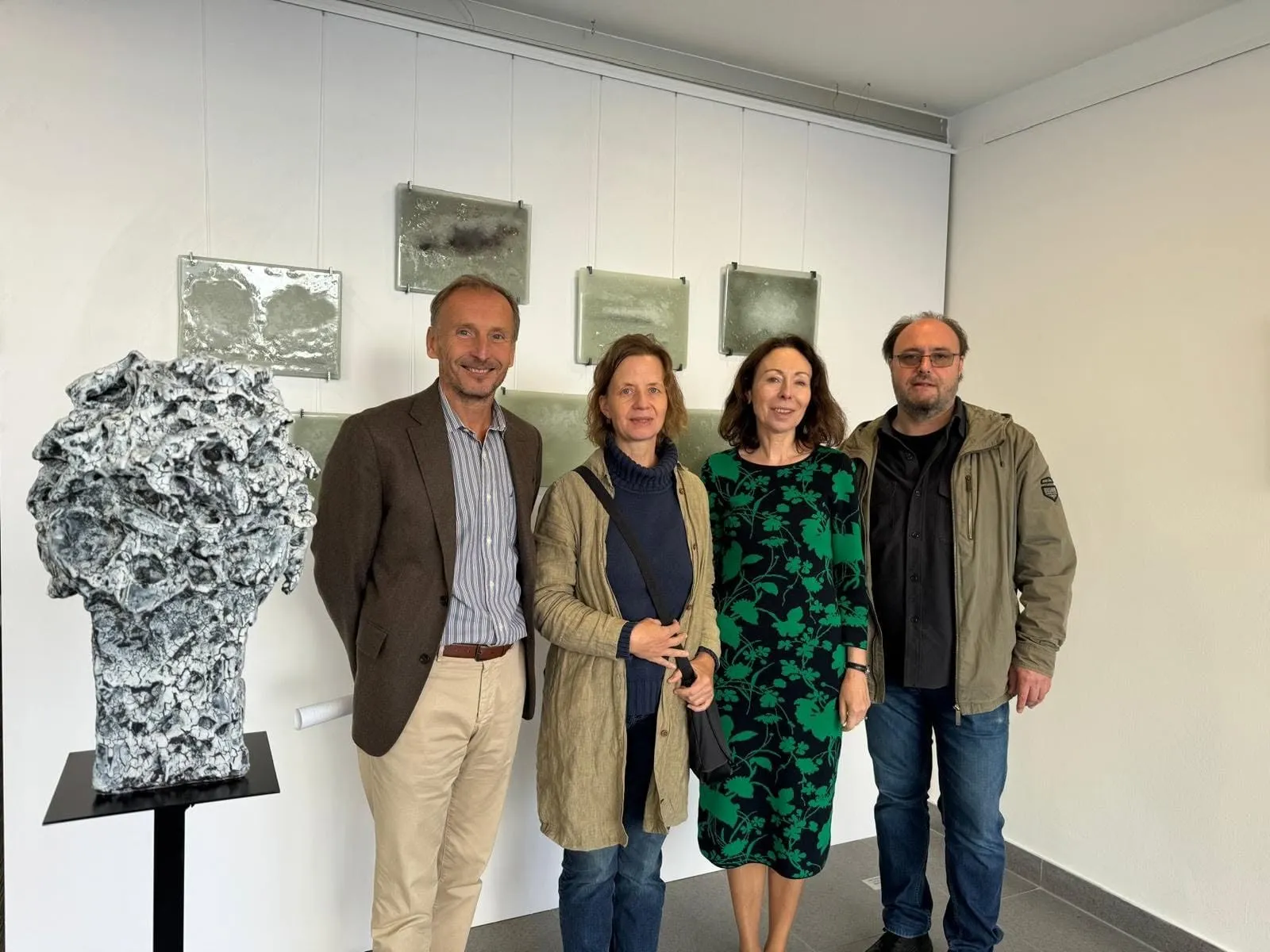 Petr Lada with three guests next to a porous ceramic head on a plinth in the exhibition space