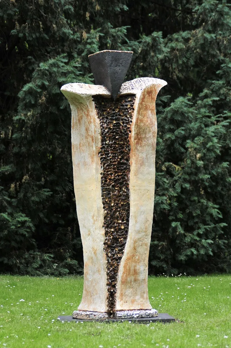Tall pale sculpture with a dark textured slit and a triangular head on a lawn