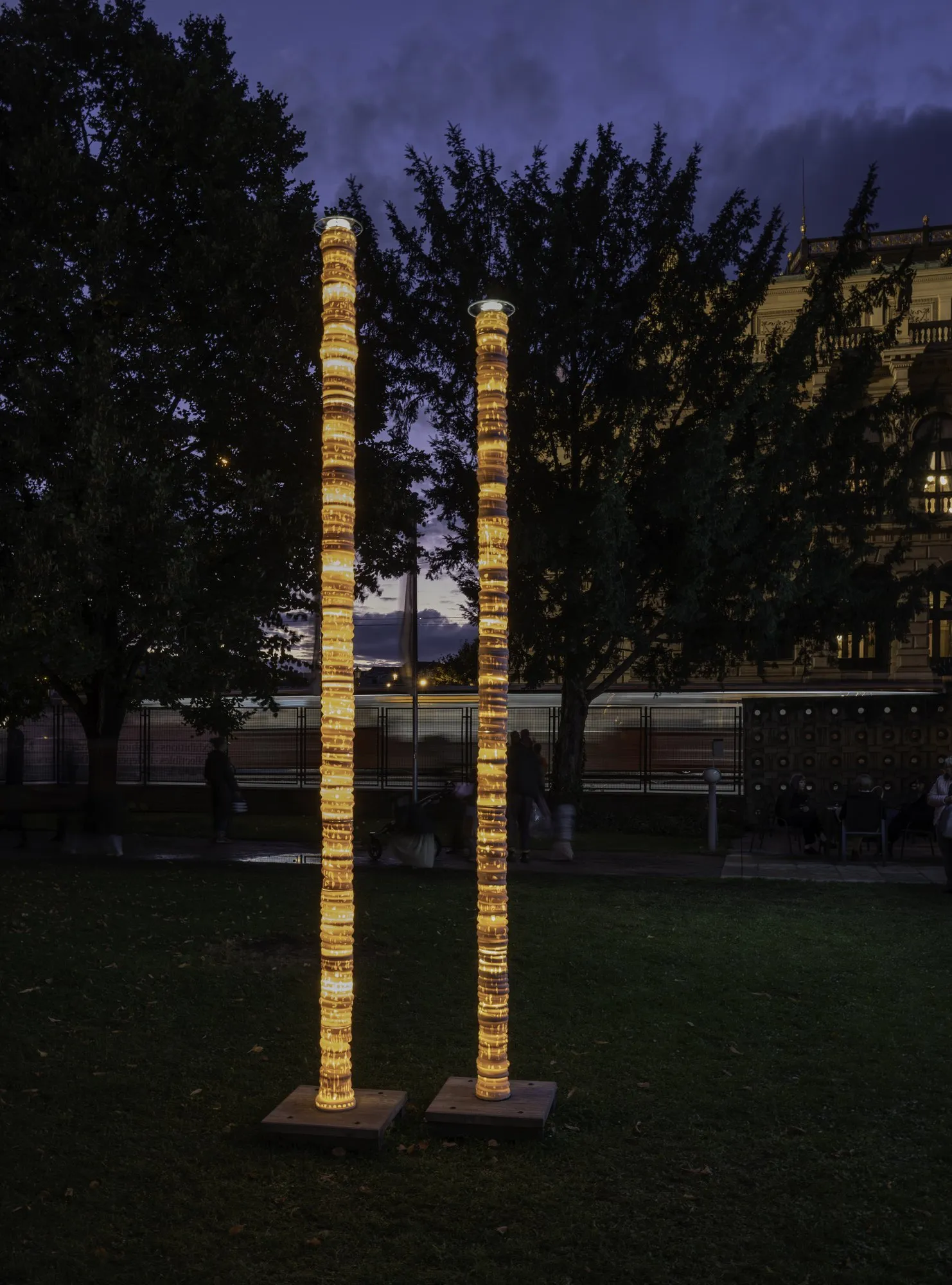 Two tall glowing porcelain columns on a lawn at dusk