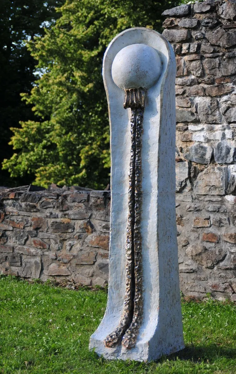 Tall white stele with a sphere on top by a stone wall