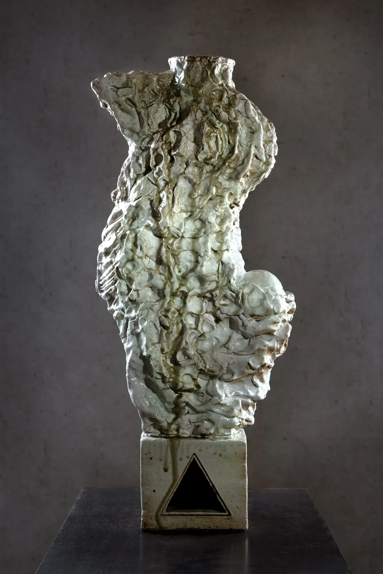 White glazed figure with green-brown drips on a plinth with a triangular opening