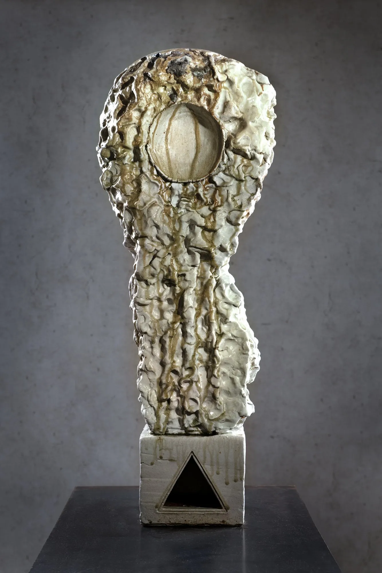 White glazed figure with a circular opening in the head on a plinth with a triangle