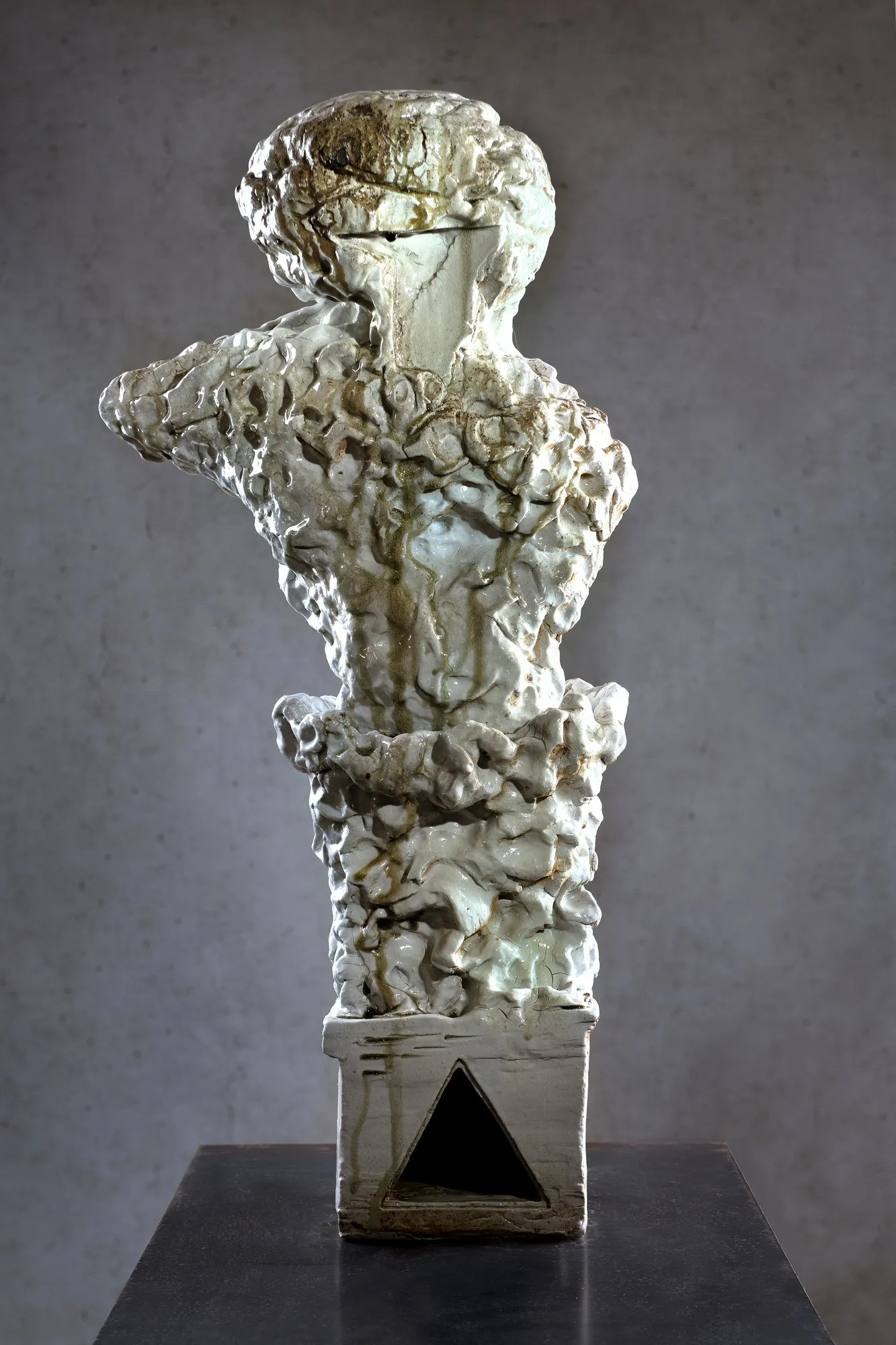 White glazed bust with green-brown drips on a plinth with a triangular opening