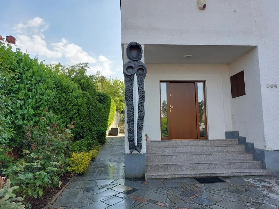 Tall dark sculpture with a circular head at the entrance of a family house